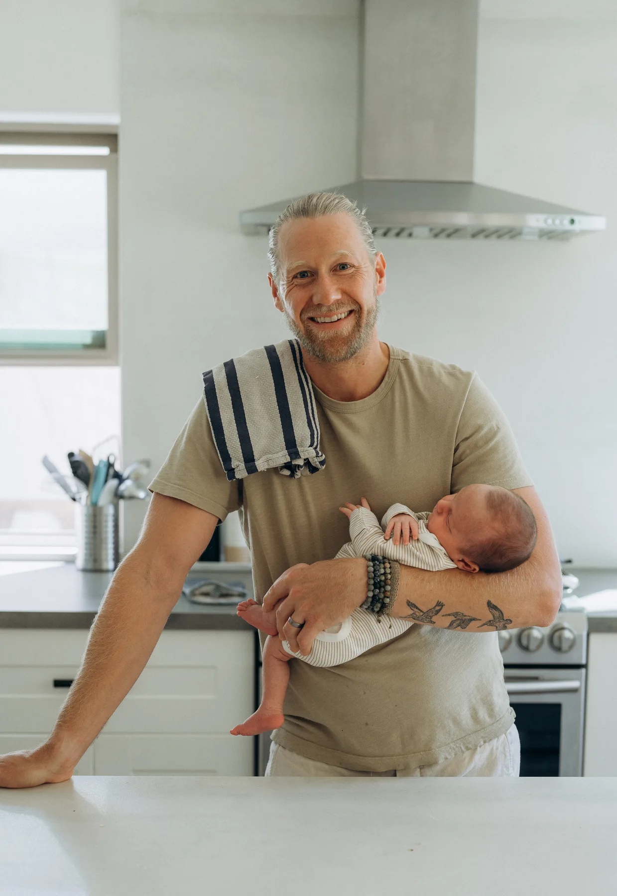 Adam smiling with his newborn in the family kitchen.