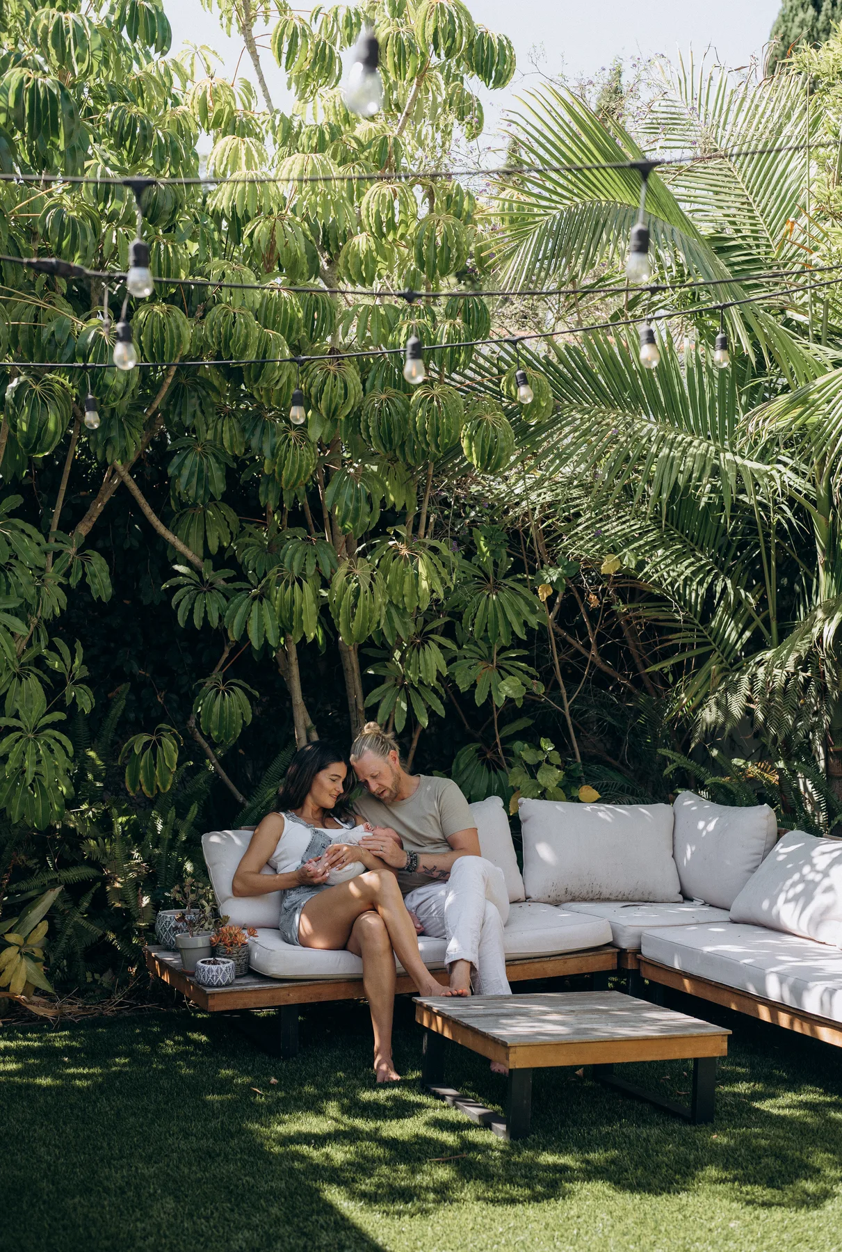 Adam and his wife sitting with their baby in the garden.