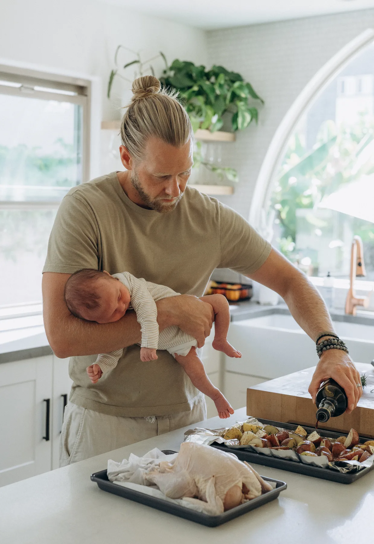 Adam prepares dinner while holding his baby in one arm.
